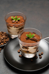 Portion of Classic tiramisu dessert in a glass cup on dark concrete background