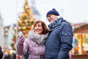 technology, winter holidays and people concept - happy senior couple taking selfie by smartphone at...
