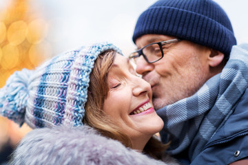love, christmas and people concept - close up of happy senior couple kissing outdoors in winter
