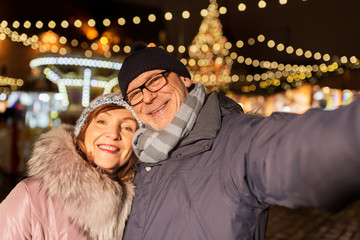 winter holidays and people concept - happy senior couple taking selfie at christmas market on town hall square in tallinn, estonia