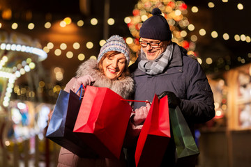 sale, winter holidays and people concept - happy senior couple with shopping bags at christmas market souvenir shop on town hall square in tallinn, estonia - Powered by Adobe