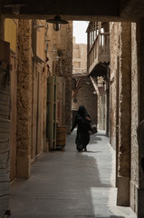 Unidentifiable Arab woman at Souq Waqif in Doha in Qatar. Muslim woman completely covered in traditional black clothing shopping at market in Doha.