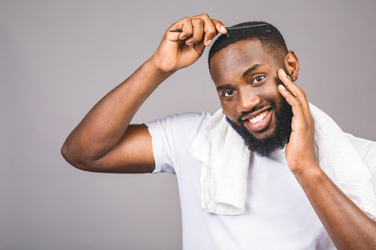 Portrait Of Handsome Young African American Black Man Combing His Hair In Bathroom. Isolated Over Grey Background.