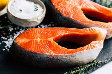 Uncooked salmon steaks on black slate background, closeup view. Raw fish ready for cooking