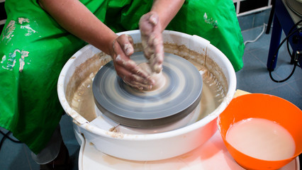 A raw clay pot in the hands of a potter. Workshop in the pottery workshop. Clay pot on a potter`s wheel