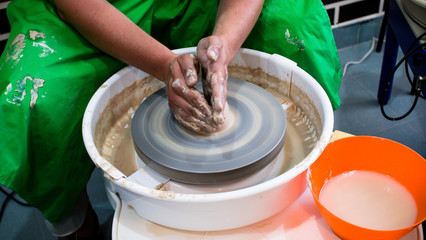 A raw clay pot in the hands of a potter. Workshop in the pottery workshop. Clay pot on a potter`s wheel