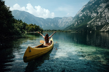 Young woman canoeing in the lake bohinj on a summer day, background alps mountains.