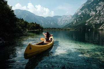 Young woman canoeing in the lake bohinj on a summer day, background alps mountains.