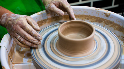 A raw clay pot in the hands of a potter. Workshop in the pottery workshop. Clay pot on a potter`s wheel