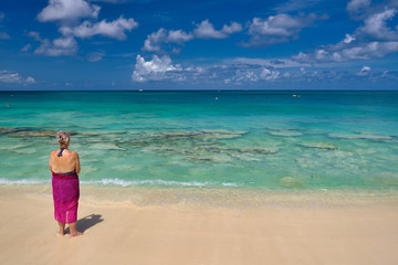 An older woman with gray hair stairs out over the crystal clear waters of the Cayman Islands in the British West Indies