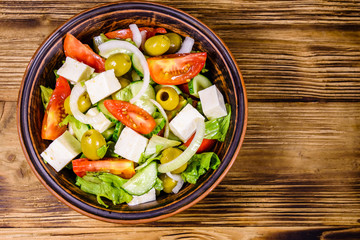 Ceramic plate with greek salad on wooden table. Top view