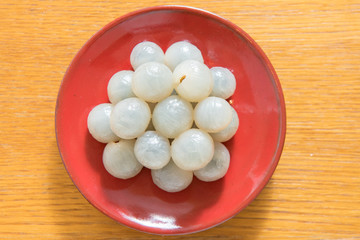 Peeled longan on a red porcelain plate isolated