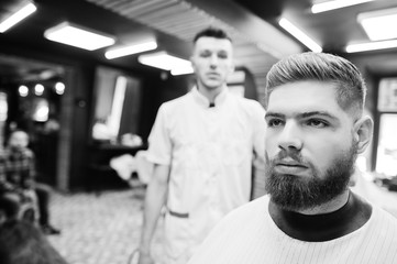 Young bearded man getting haircut by hairdresser while sitting in chair at barbershop. Barber soul.