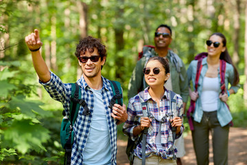 travel, tourism, hike and people concept - group of friends walking with backpacks in forest