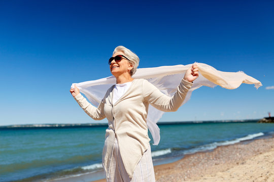 People And Leisure Concept - Portrait Of Happy Senior Woman In Sunglasses With Waving Scarf On Beach In Estonia