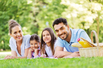 family, leisure and people concept - happy mother, father and two daughters laying on picnic...