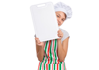 Happy teen girl in chef hat holding cutting board, isolated on white background. Portrait of cute smiling child cook in apron showing cutting board with space for text. Tools and equipment for cooking