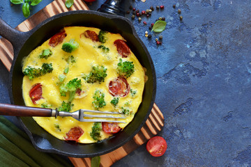 Omelet with vegetables in a cast-iron pan on the table.