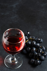 Red wine in a glass, a bunch of grapes. Dark background. Copy space
