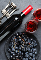 Red wine in glasses, grapes, bottle of wine, corkscrew. Dark background.