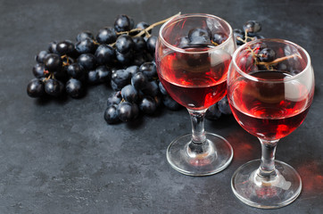 Red wine in glasses, a bunch of black grapes. Dark background. Copy space
