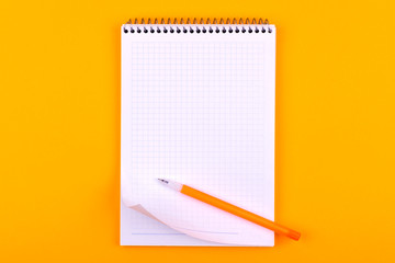 Notebook on a spring with white sheets of paper for drawings, texts and notes, next to a yellow pen lies on an orange background