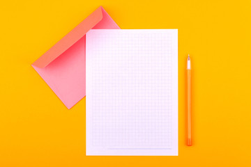 A white sheet of paper with a notebook for drawings, texts and notes, next to a yellow pen and an envelope for letters, lie on an orange background
