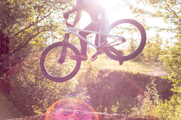 young guy athlete, training makes jumps and bike stunts in the forest, against the setting sun....