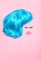 Blue wig with eyelashes and paper lips on pink background. Minimalism concept