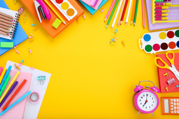 Different school supplies with alarm clock on yellow background