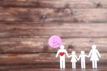 Family figures with red heart and speech bubble on brown wooden background