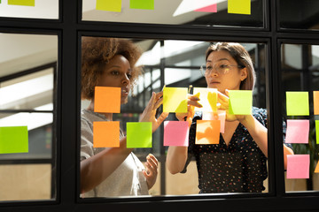 Serious african and asian female coworkers working with sticky notes