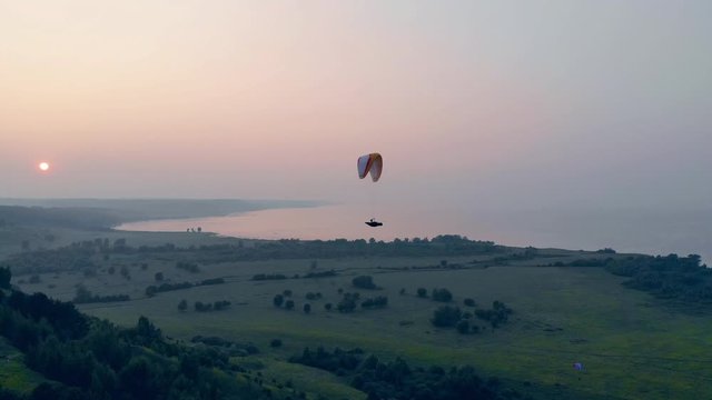 Athlete flying on a paraglider in sky on a sunset background. Paragliding, action, extreme sport concept.