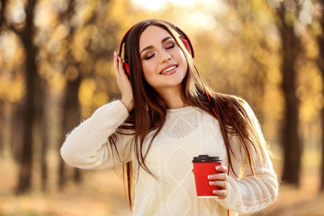 Beautiful woman with headphones and paper cup in autumn park