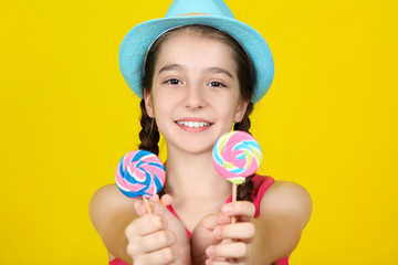Beautiful young girl with sweet lollipops on yellow background