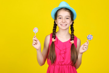 Beautiful young girl with sweet lollipops on yellow background
