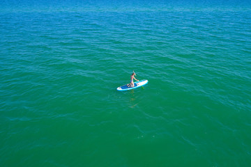 Aerial drone birds eye view of young woman exercising sup board in turquoise tropical clear waters