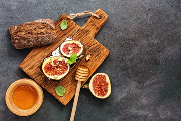 Sandwich with figs, cream cheese, honey and mint leaves on a cutting board, dark rustic background. Top view, flat lay.