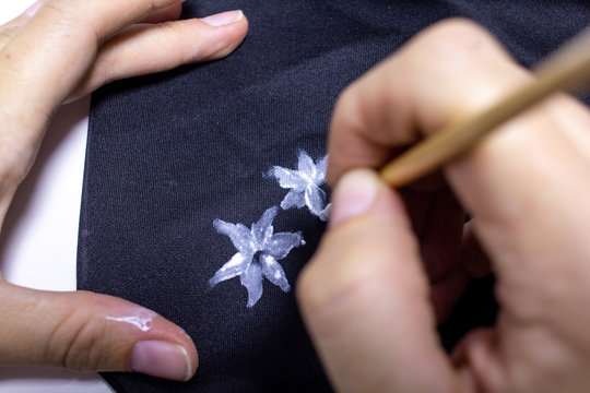 A woman paints on black fabric white flowers with a brush. DIY. Painting with a brush. White painted flowers. Painting on fabric.