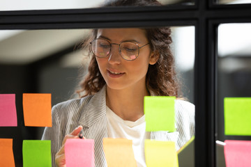 Young businesswoman write ideas on sticky notes on glass board