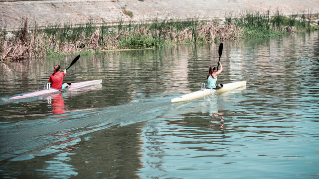 Two young women athletes on rowing kayak on lake, competition
