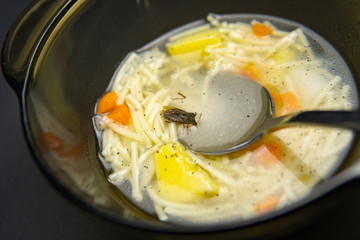 Hot soup with steam in the soup, a spoon in a silver and aluminum black glassware on a dark background.