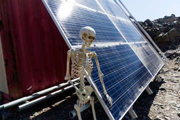 Skeleton leaning on solar panels in the desert