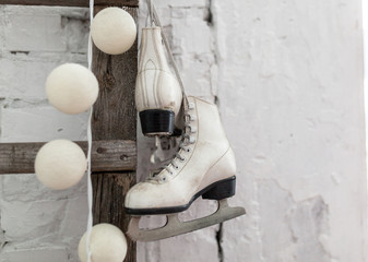 Figure skates and Christmas garland lights on old white brick rustic background.