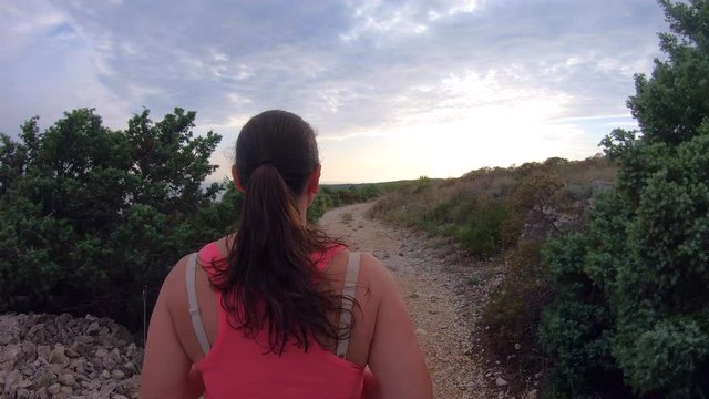 TS Woman running on a dusty trail above the Adriatic Sea at sunset