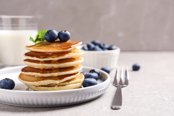 Plate of tasty pancakes with blueberries and honey on light grey table. Space for text