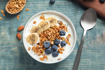 Bowl of yogurt with blueberries, banana and oatmeal on color wooden table, flat lay