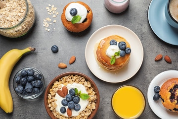 Different tasty dishes with blueberries on grey table, flat lay