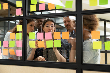 Focused multiethnic business team brainstorm with sticky notes in office