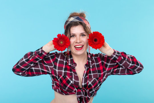 Close-up portrait of a beautiful young woman holding red flowers with different hearts in the hands posing on a blue background. Concept of differences and delicate nuances.